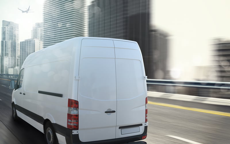 White van moving fast on the highway with a modern city in the background