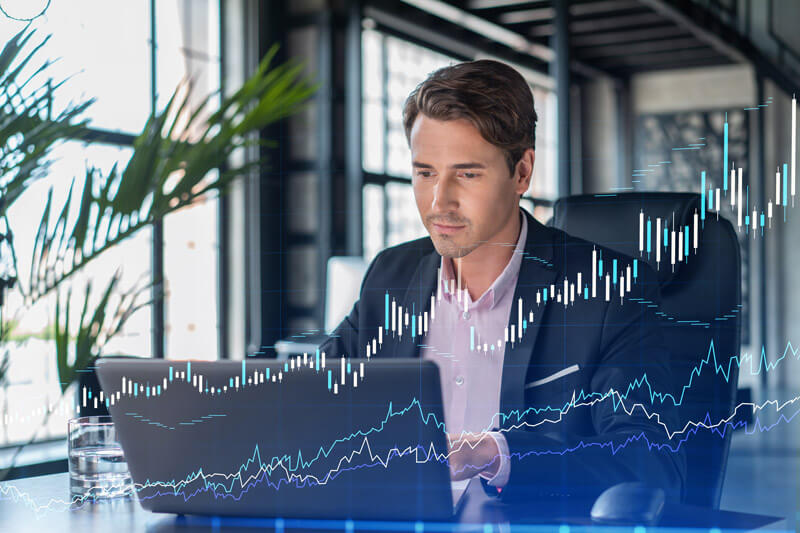 A man works on a laptop with line graphs trending upward overlaying the image