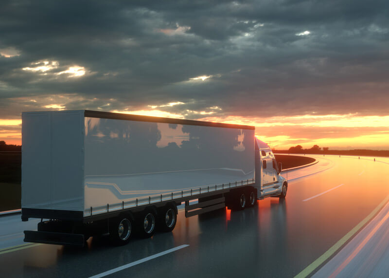 A semitruck drives down the highway at sunset