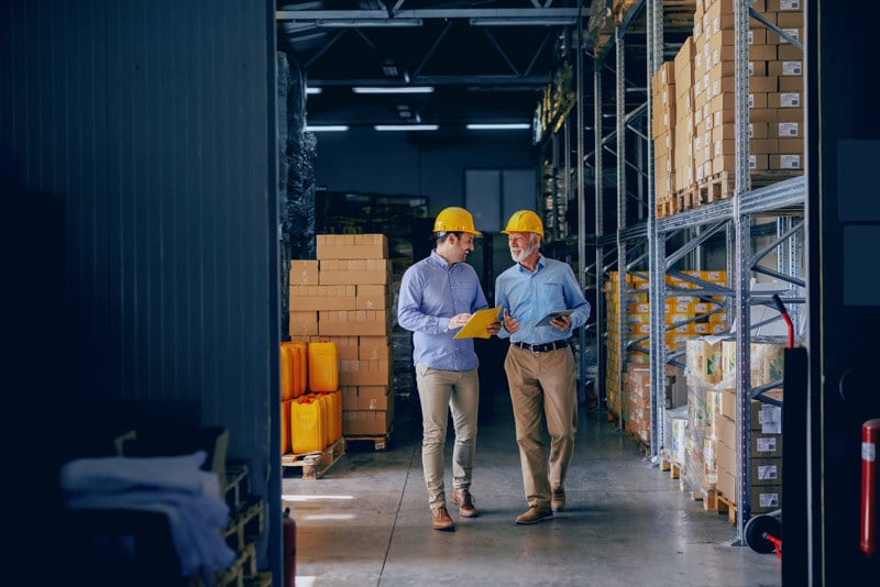 two men walking through warehouse wearing hardhats