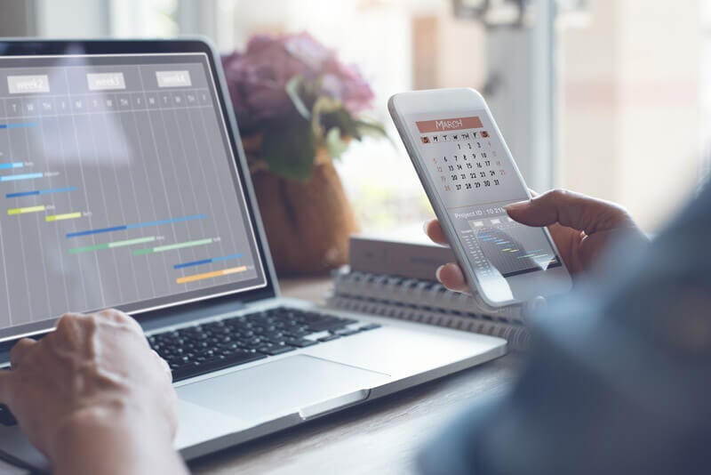 Closeup of someone using a laptop and phone to manage a schedule