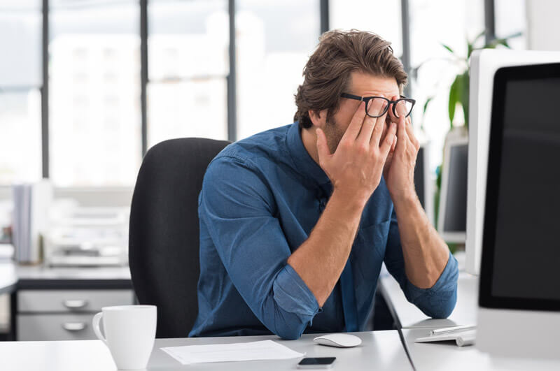 A customer service rep sitting at a desk with his head in his hands